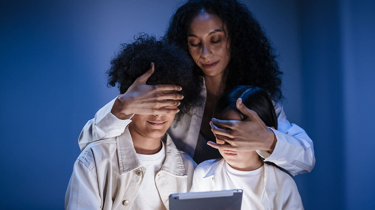 Mother covering eyes of her children with hands against internet content on digital pad