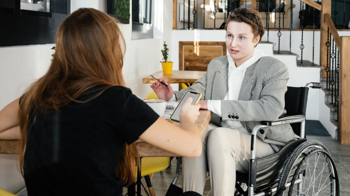Women in wheelchair communicating with female colleague in cafe