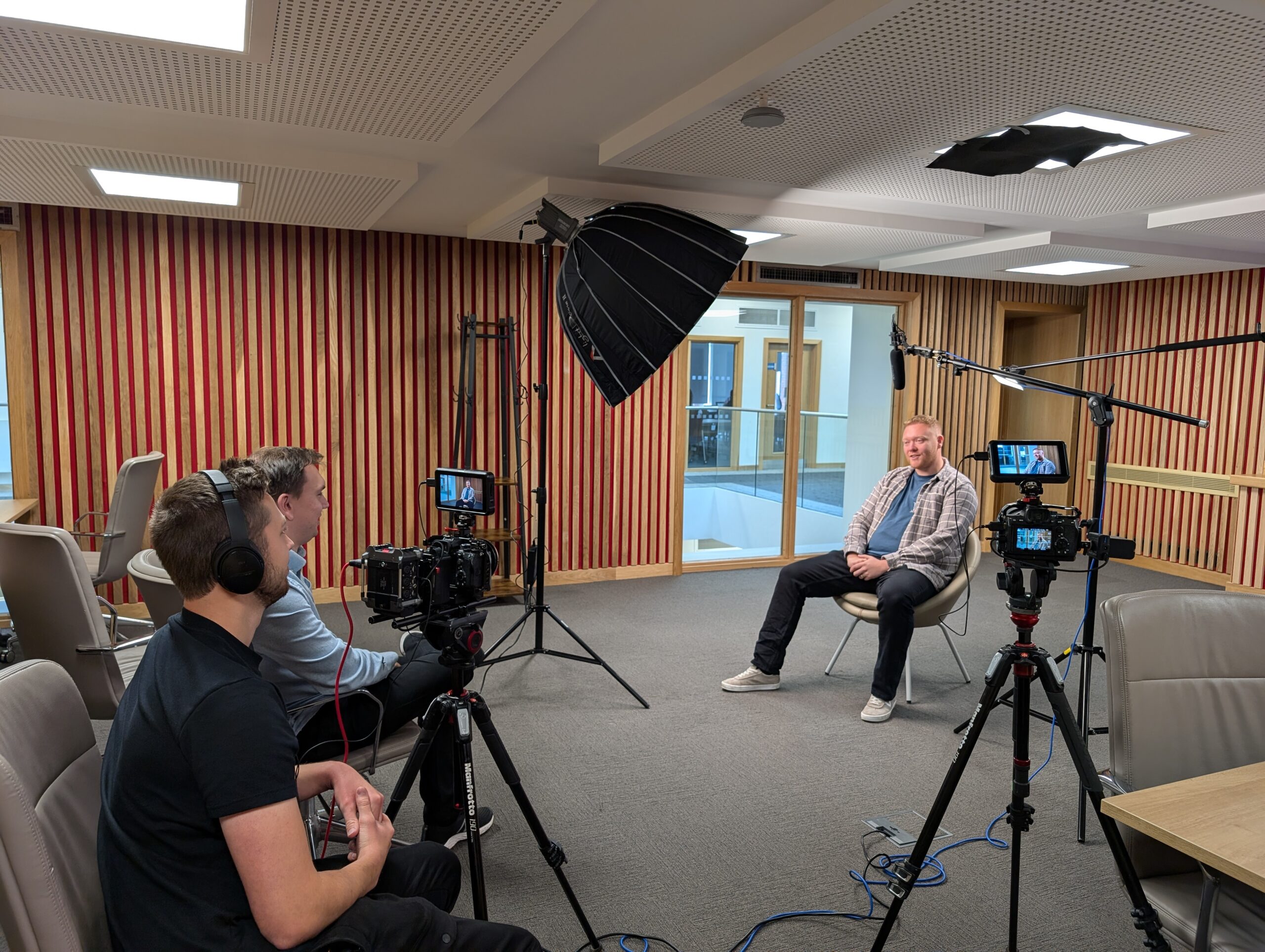 Behind-the-scenes of a testimonial video shoot at Newman University, featuring a professional setup with lighting, cameras, and an interviewee seated in a modern space.