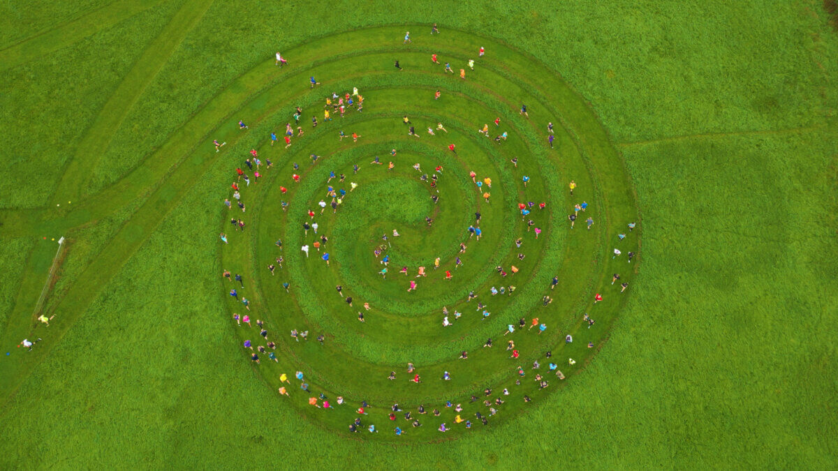 Aerial view of a large group of people forming a colorful spiral pattern on a lush green field.