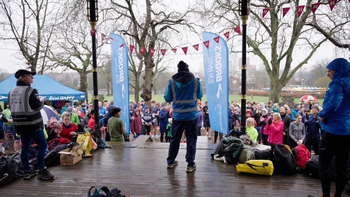 Community members gathered at a local park event, listening attentively to a speaker at the podium under event banners.