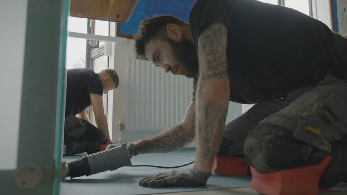 Two craftsmen intently working on installing flooring as part of a video production project under a retainer agreement.